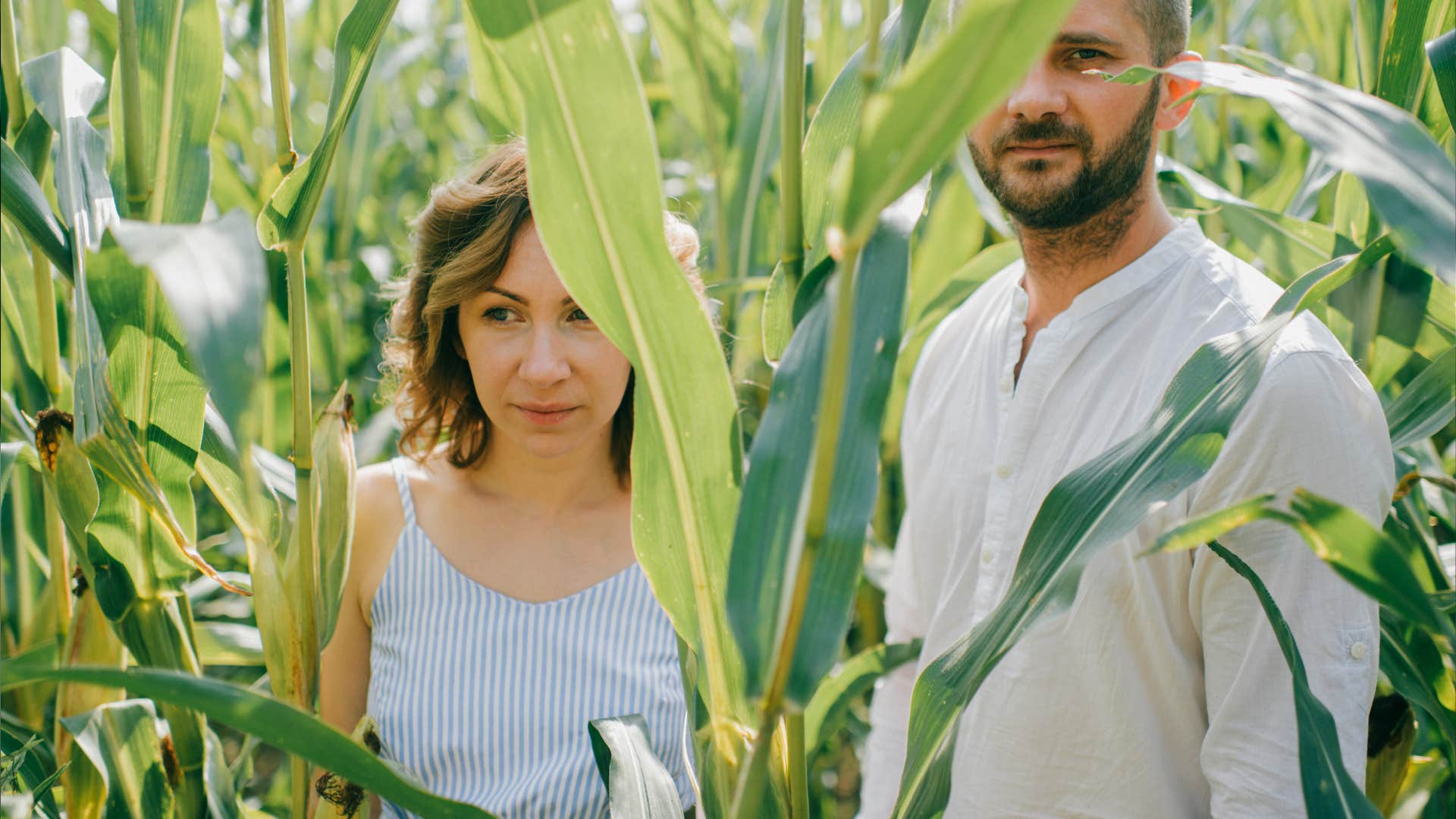 woman with short dark hair in blue dress with her husband relaxes together in the village cornfield.