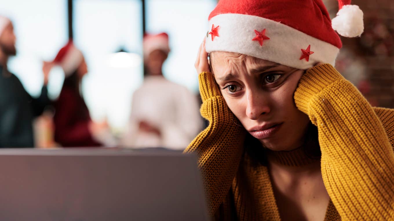 sad, lonely employee working on laptop with Santa hat on