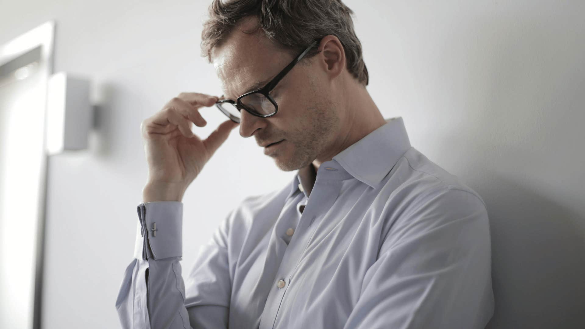 man looking down with his hand on his glasses