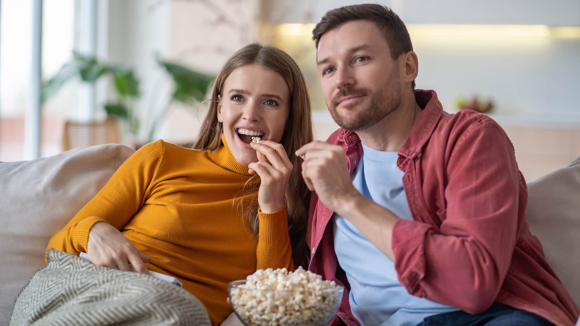 Couple smiling and watching TV together on the couch.