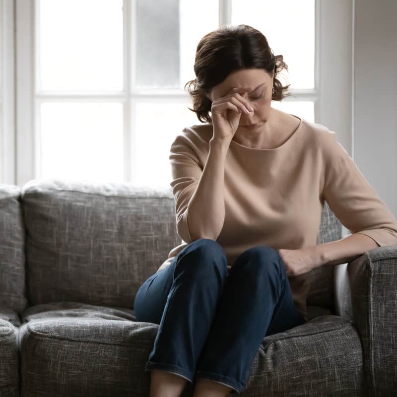 Upset middle-aged woman sitting on couch lost in thought