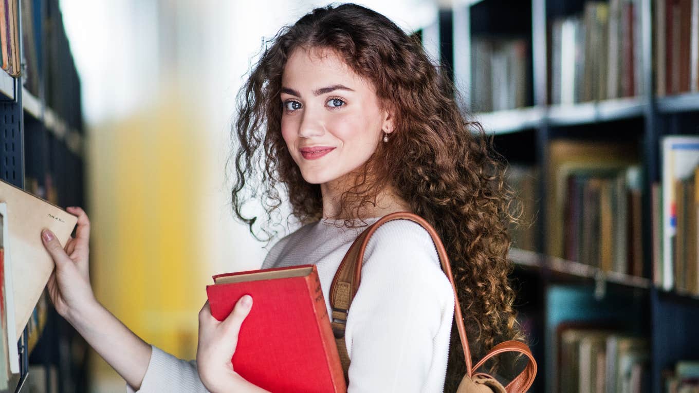 Young female student in library, looking for books, preparing for final exam.