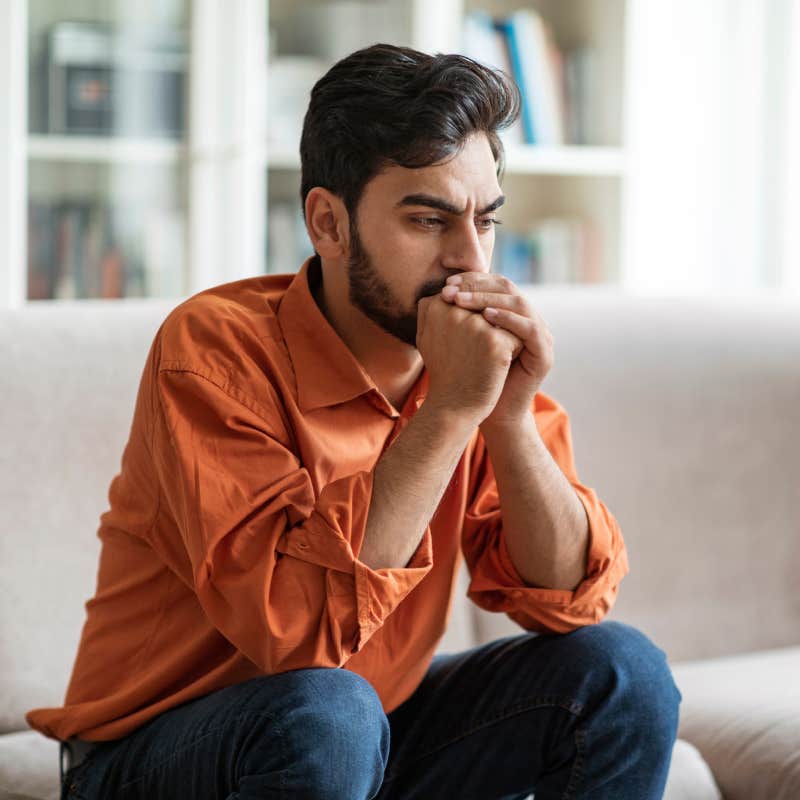 serious man sitting on sofa with hands over mouth