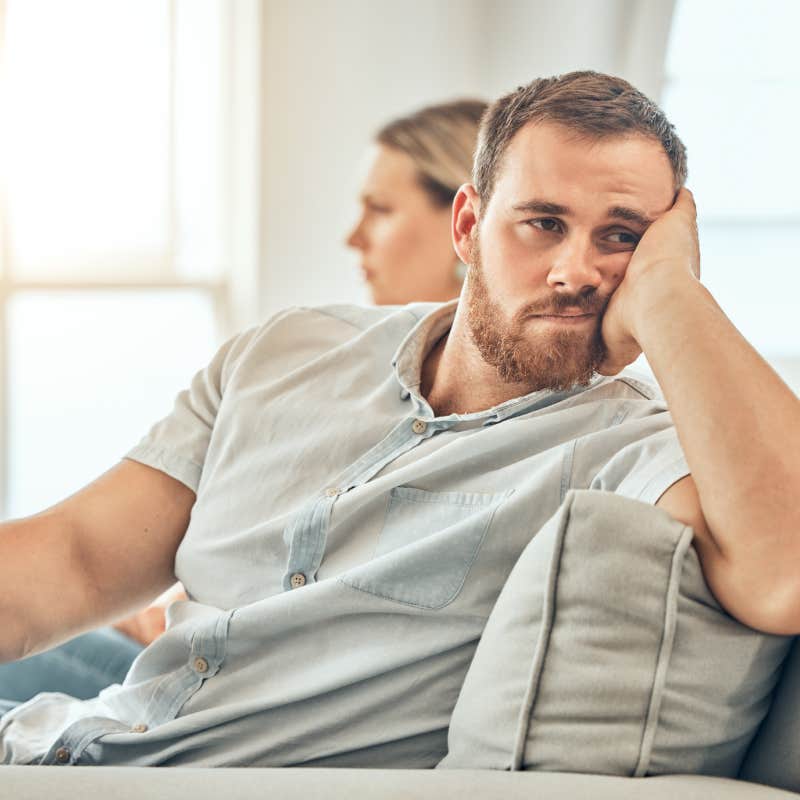 Young caucasian man with a beard looking unhappy and annoyed while sitting on the couch during an argument with his wife at home