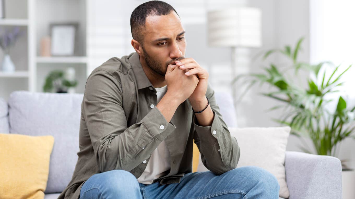 young man sitting thoughtfully and upset at home on the couch.