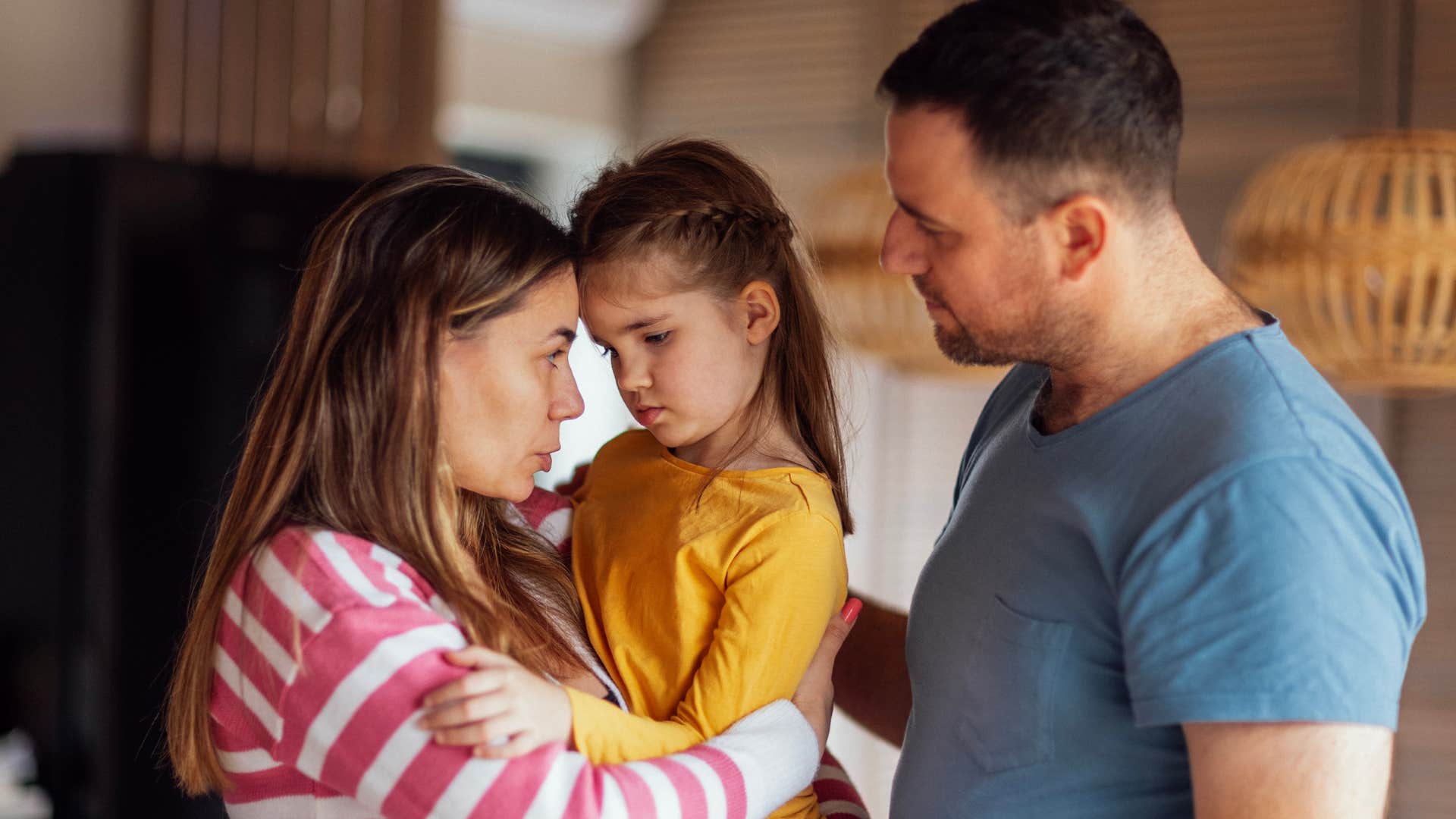 Parents hugging their upset young daughter.