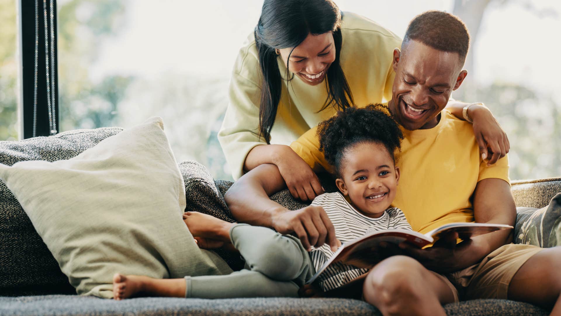 Family smiling and reading with their young daughter.