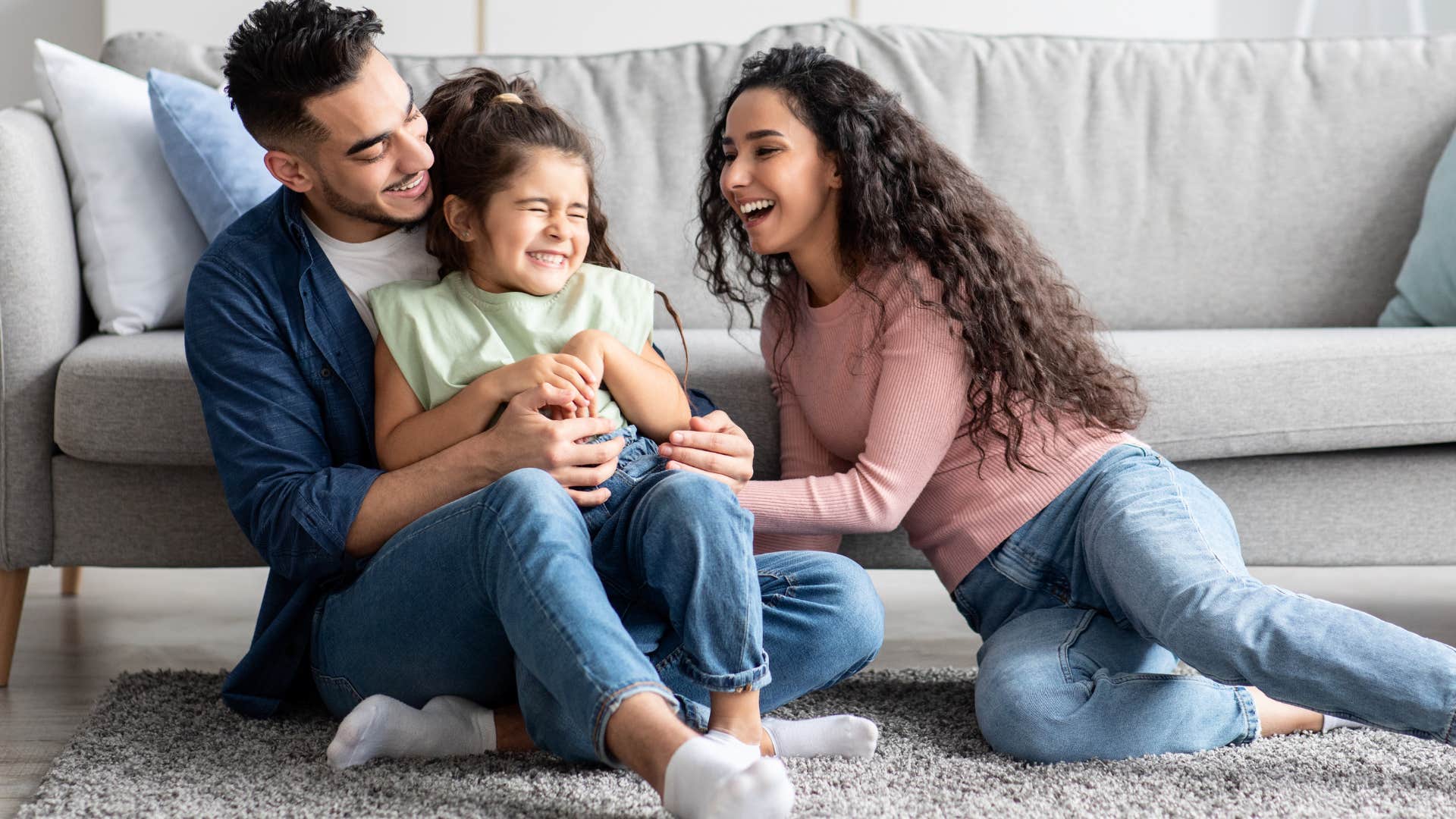 Two parents hugging their smiling young daughter.