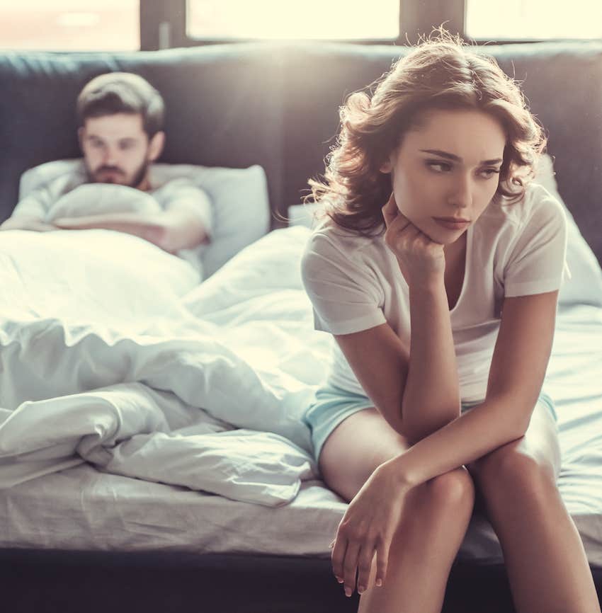 Betrayed woman sits on bed while man ignores her