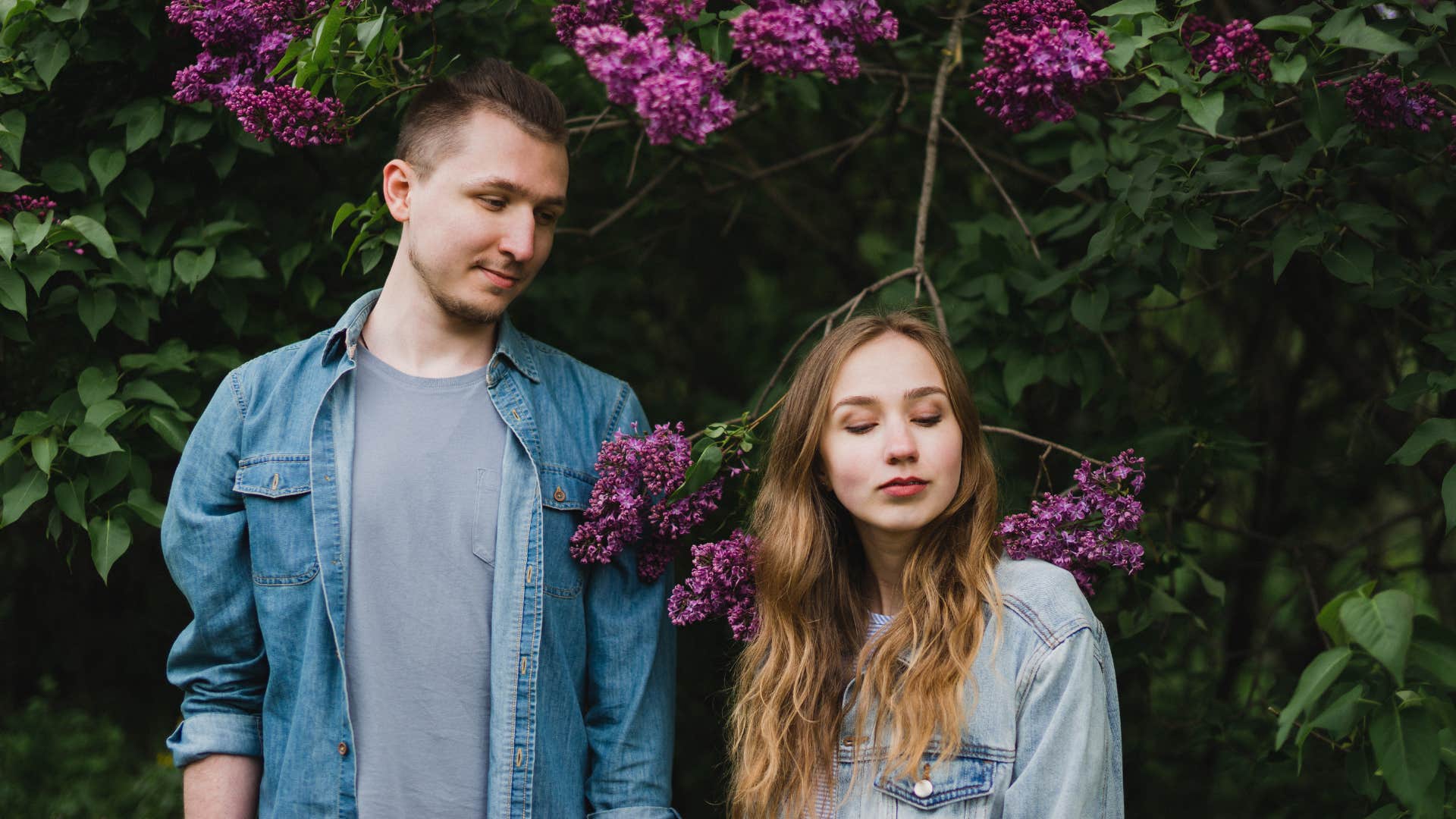 casual couple standing by purple flower hedge