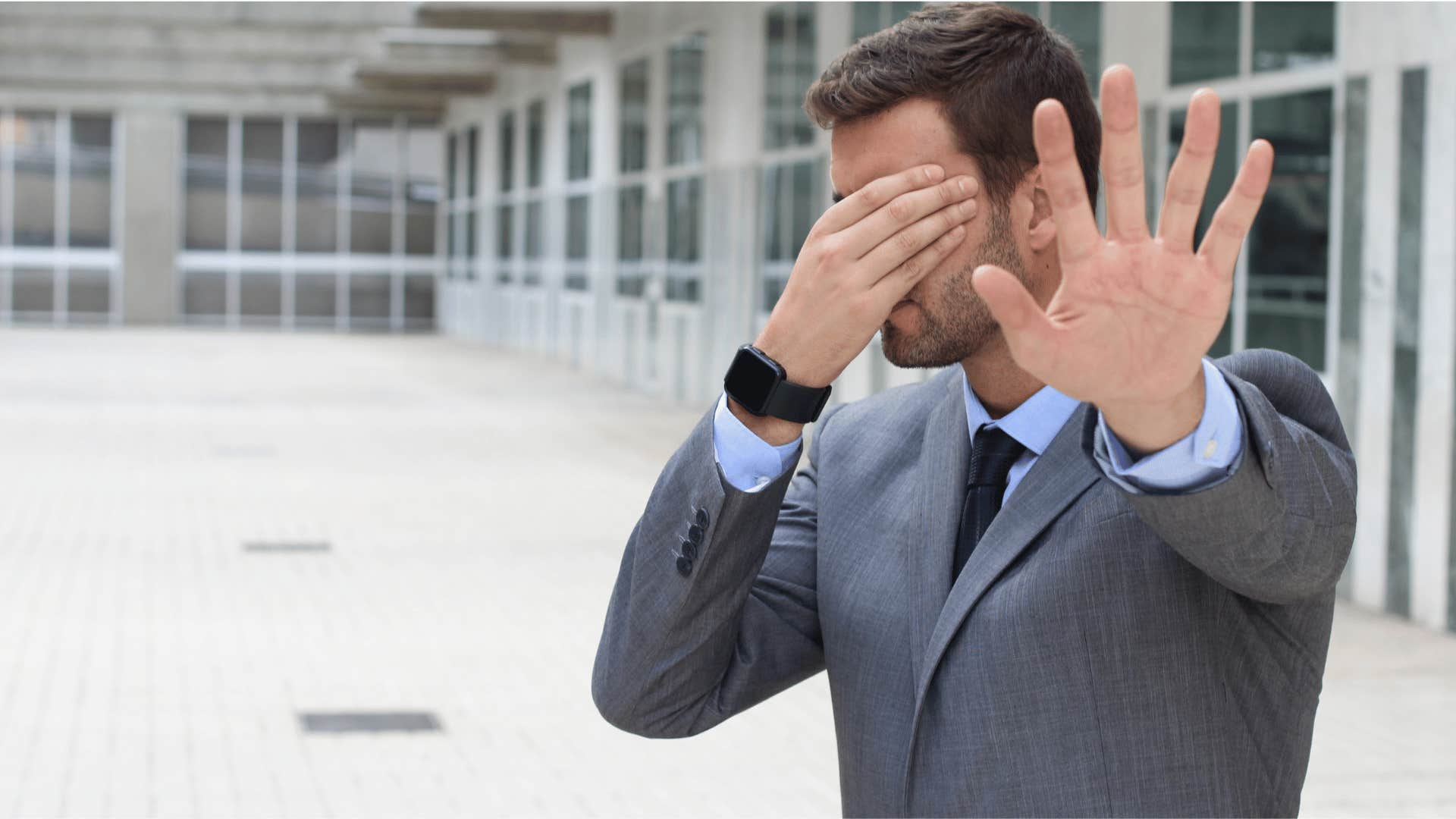 man covering his face and holding up his hand 