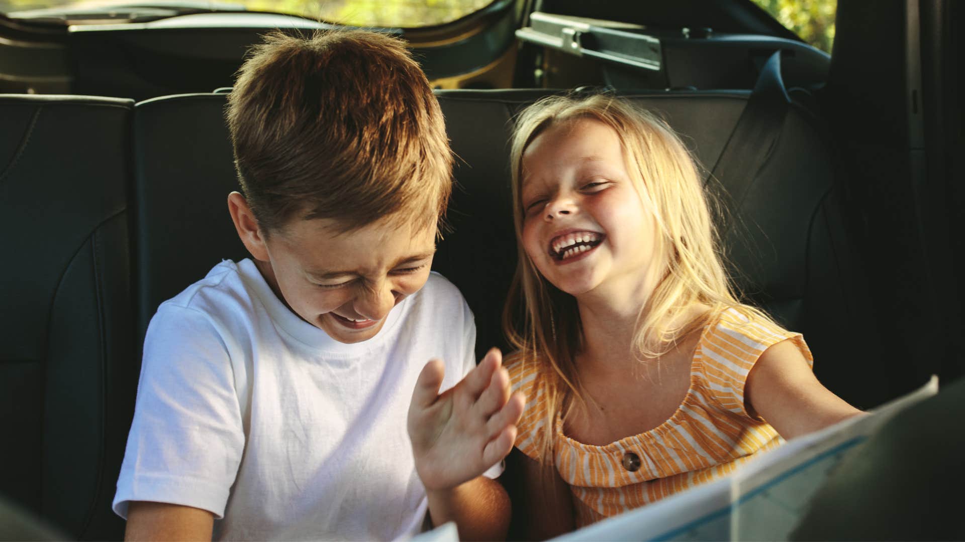 Little kids smiling and laughing in the backseat of a car