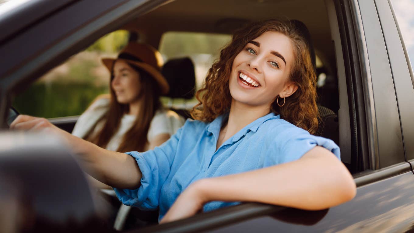 Two women smiling in a car together on a road trip.