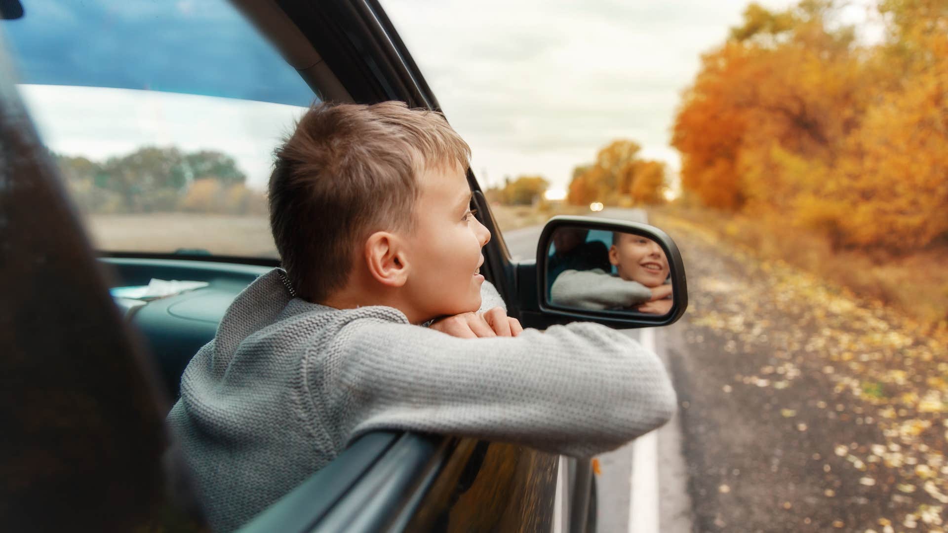 Little kid smiling with his head out a car window