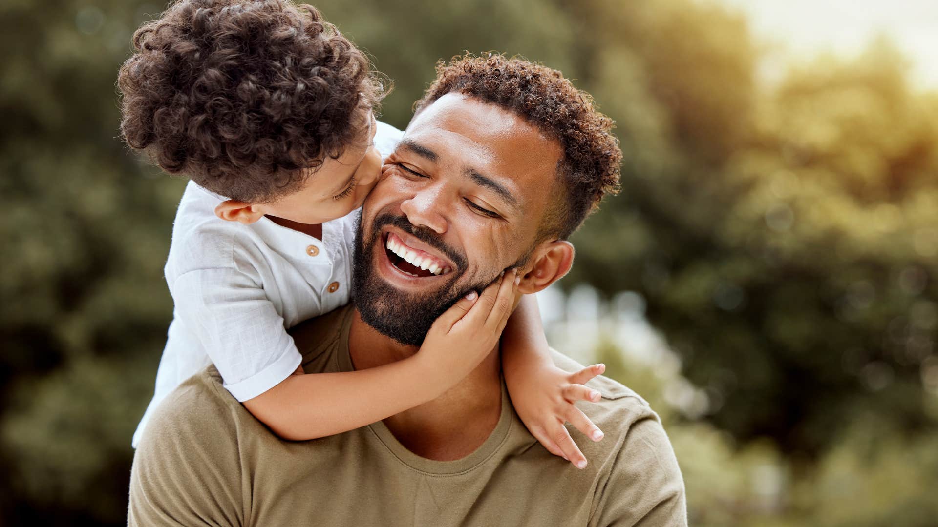 Smiling dad getting kissed on the cheek by his son.