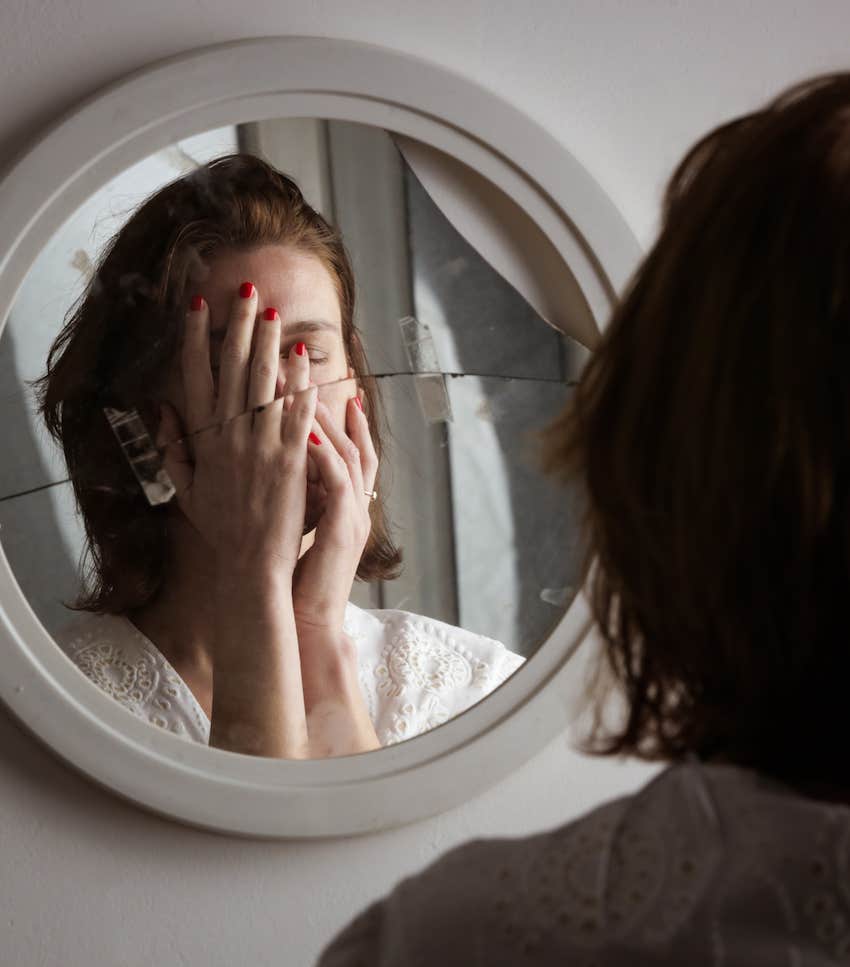 Shattered mirror reflects woman covering her face with her hands