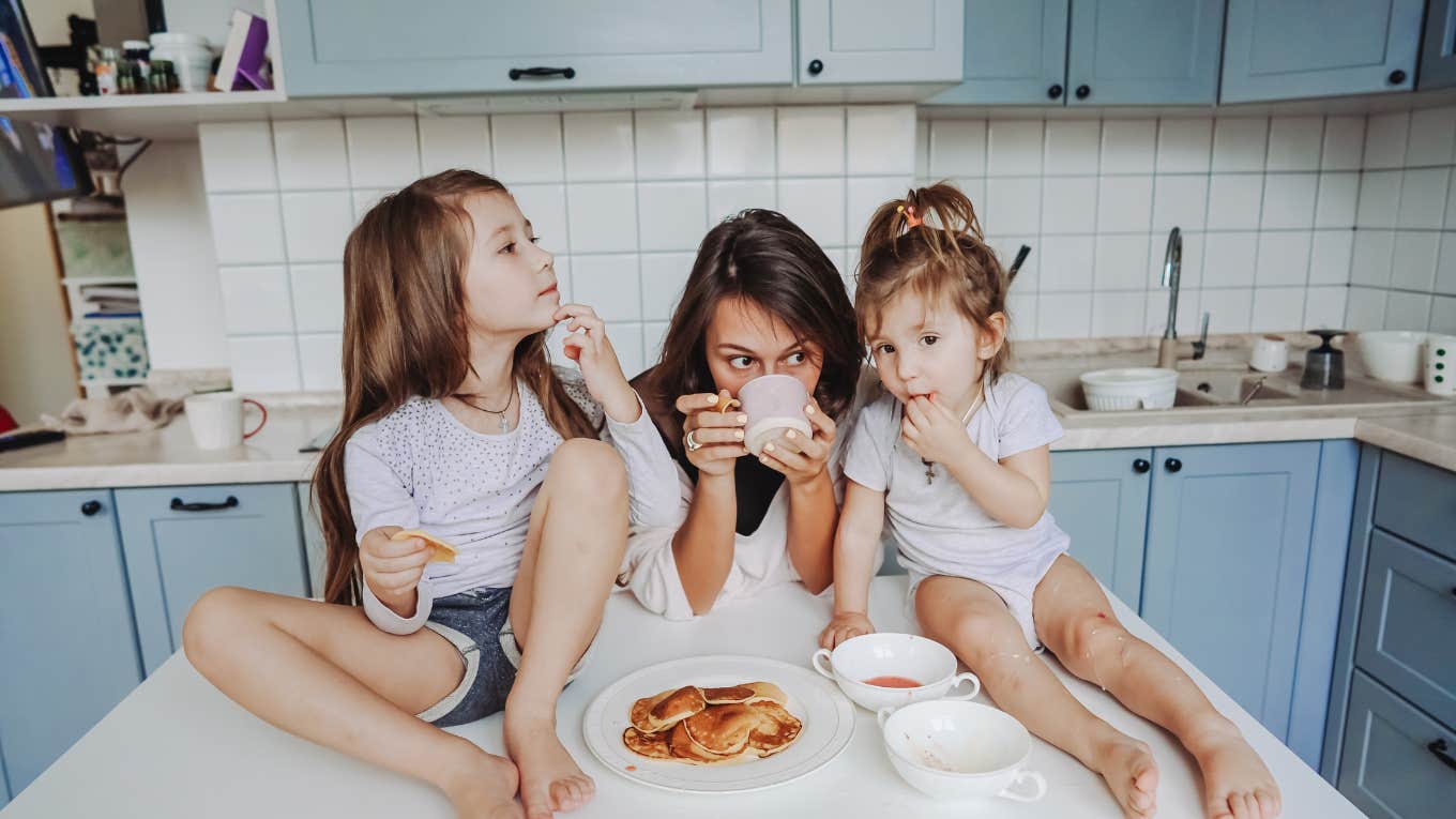 mom drinking coffee in the kitchen with two young kids