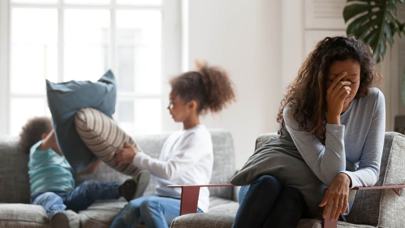 overwhelmed mom sitting while kids play behind her