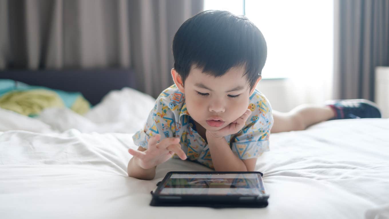 little boy lying on bed using tablet