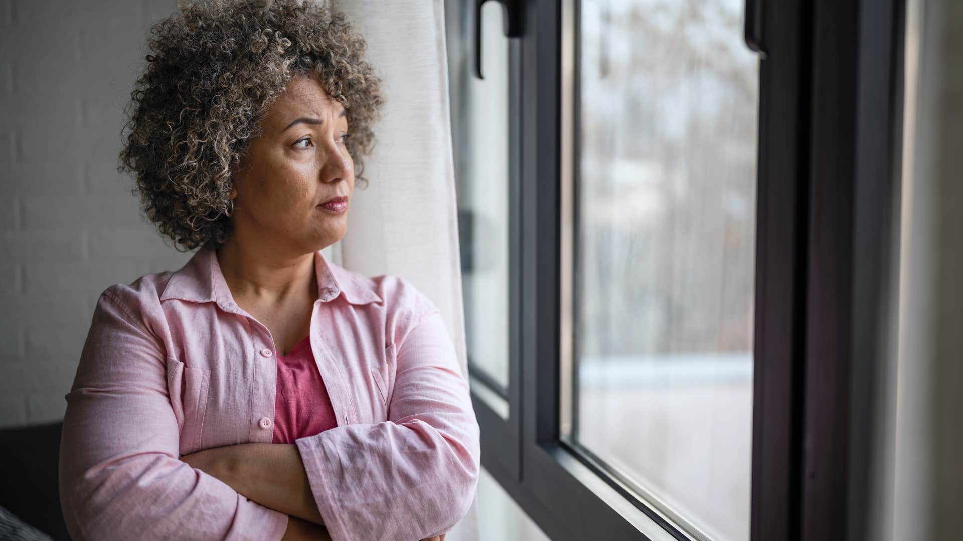 Older woman crossing her arms and looking out the window.