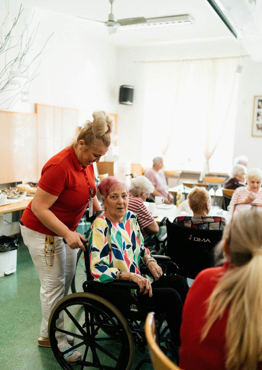 nurse pushing someone in a wheelchair in a nursing home