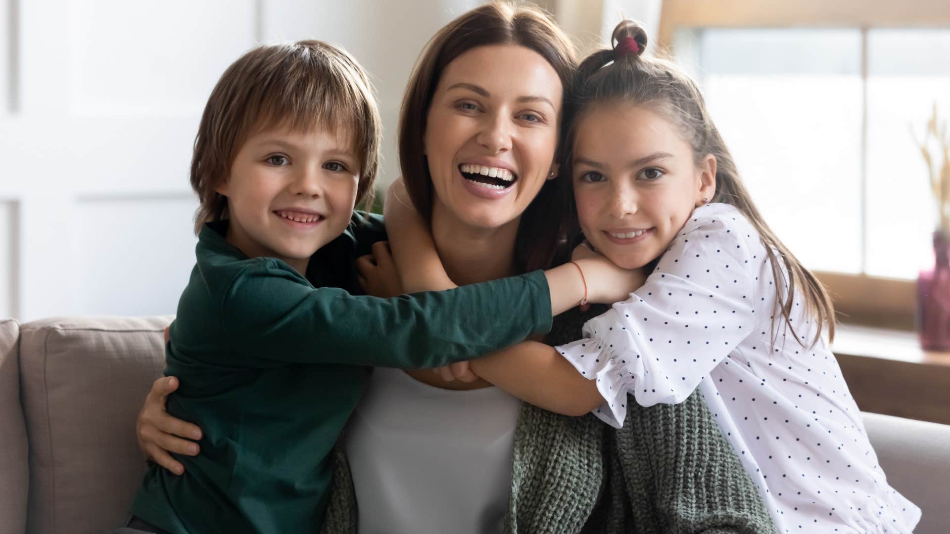 Mom smiling and hugging her two young kids.