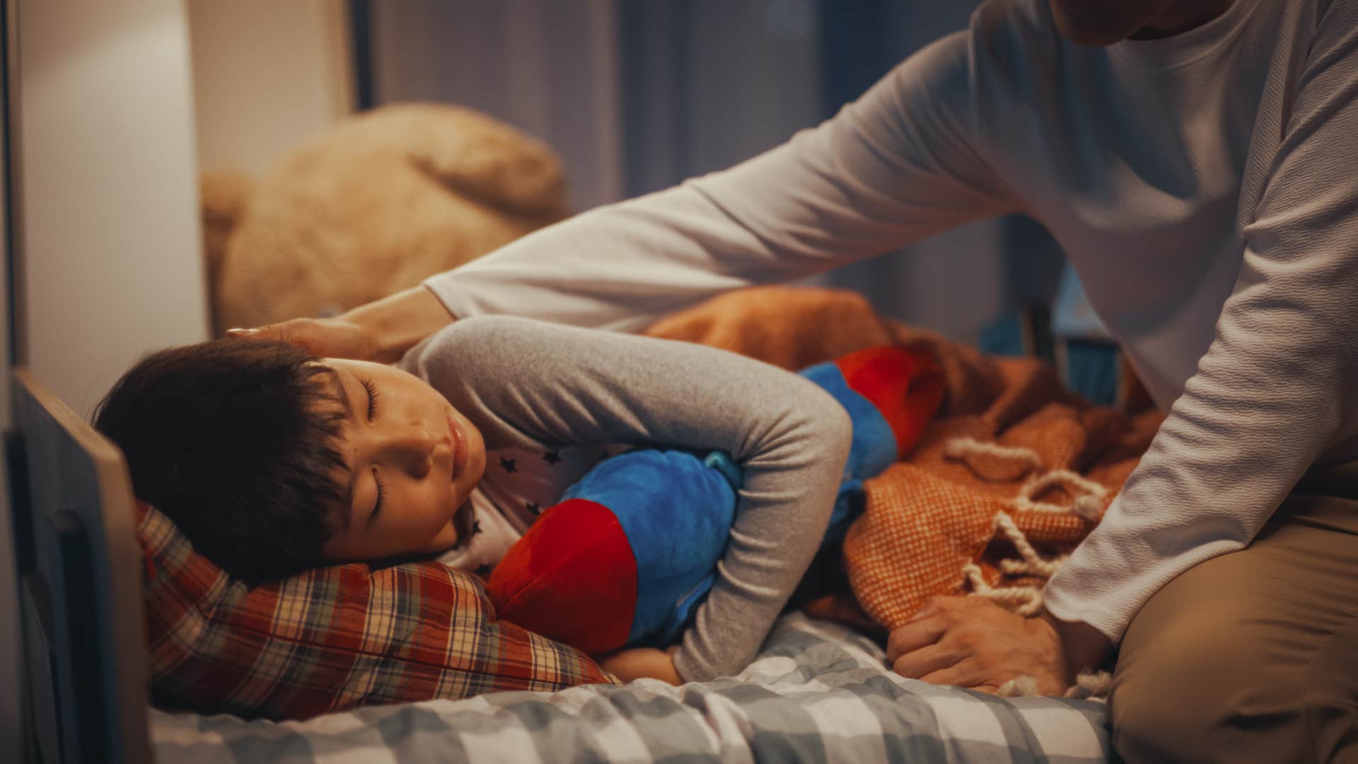 Young boy laying in his bed by his mom.