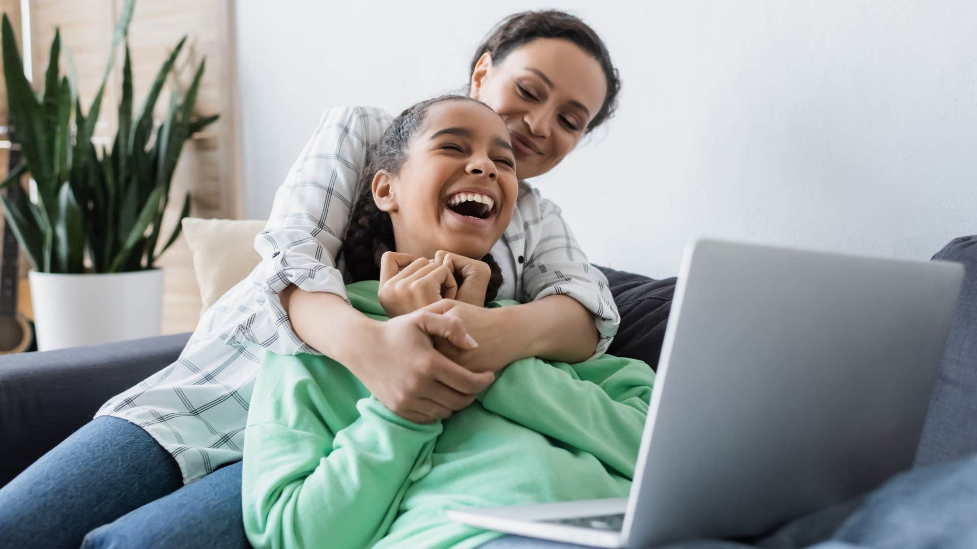 Mom hugging her teenage daughter in front of her laptop.