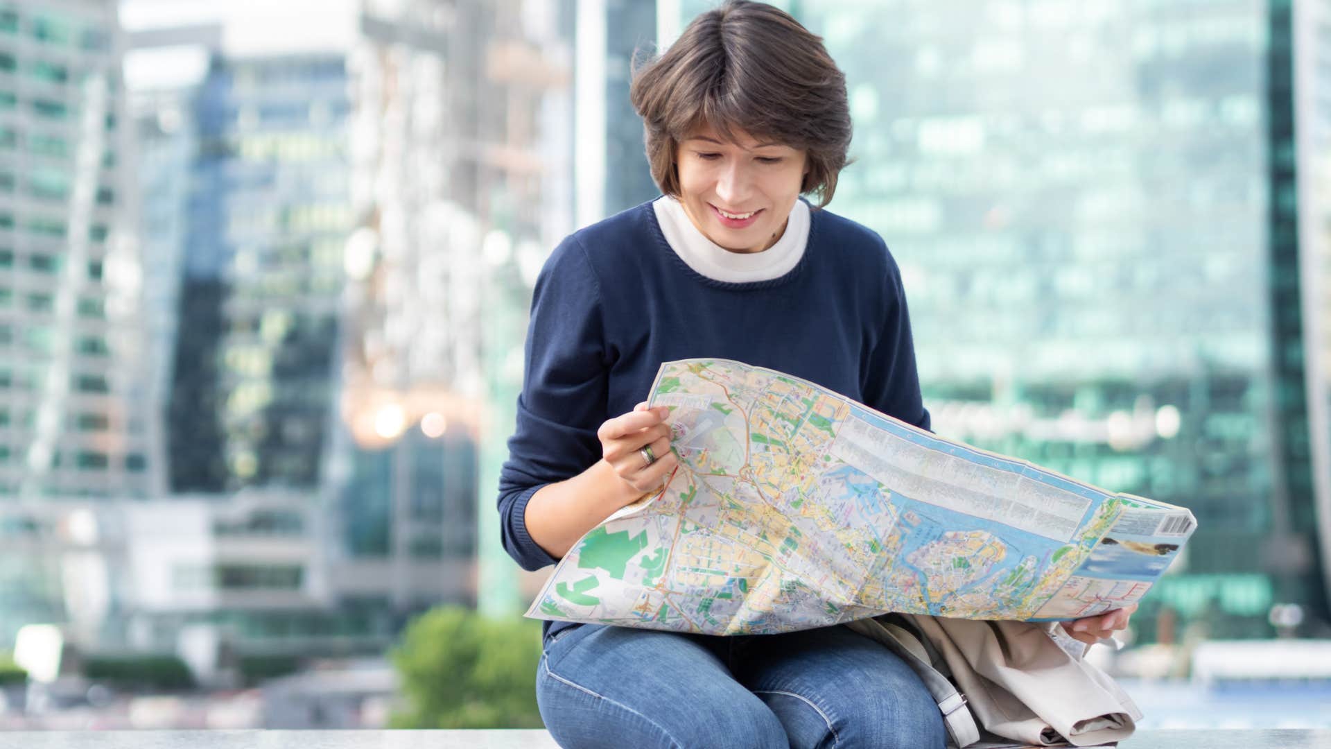 Woman sitting on a ledge reading a paper map. 