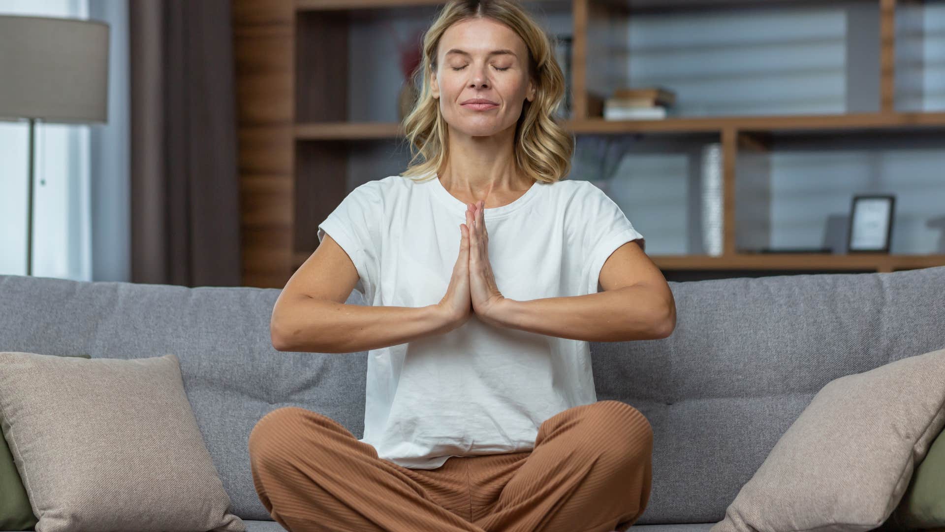 Woman sitting on her couch meditating with her eyes closed.