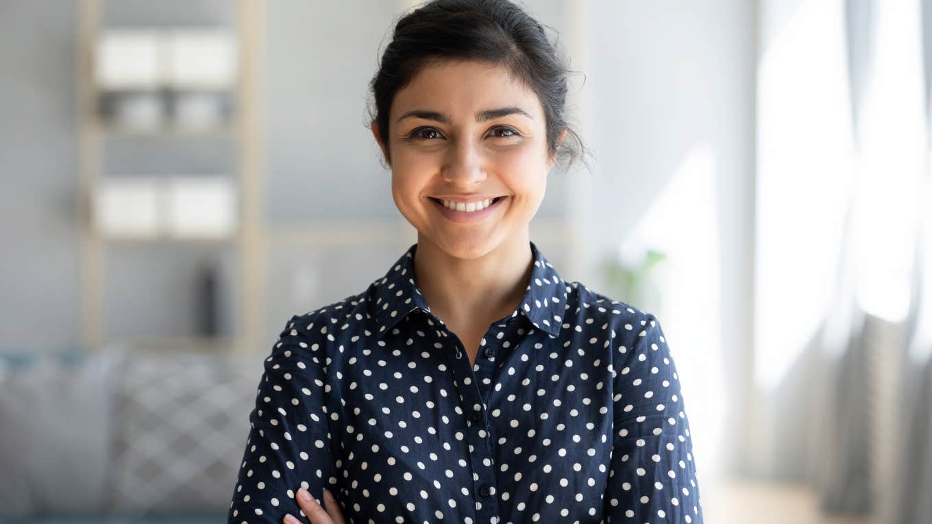 Millennial woman smiling with her arms crossed at work. 