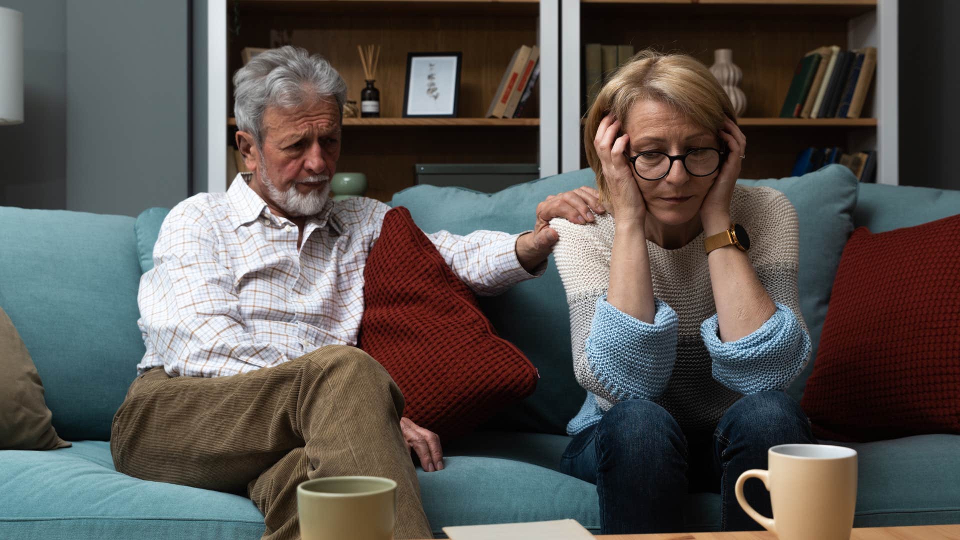 Upset older couple sitting on their couch together.