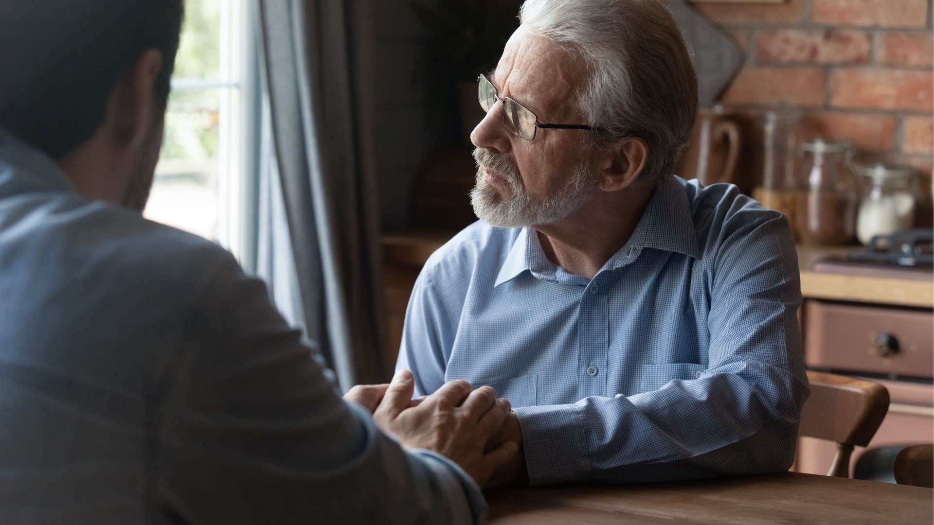 Older man looking upset holding his adult son's hand.