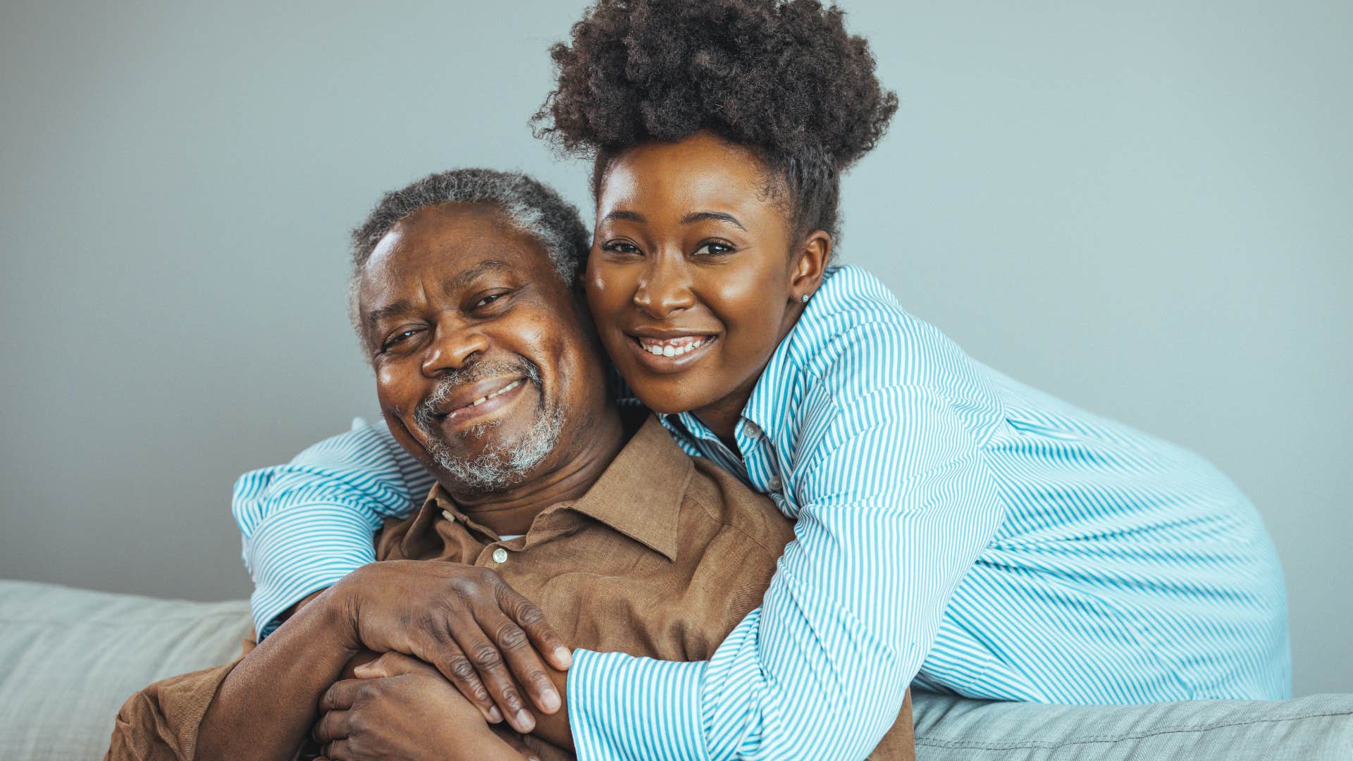 Adult daughter hugging her older dad on the couch.