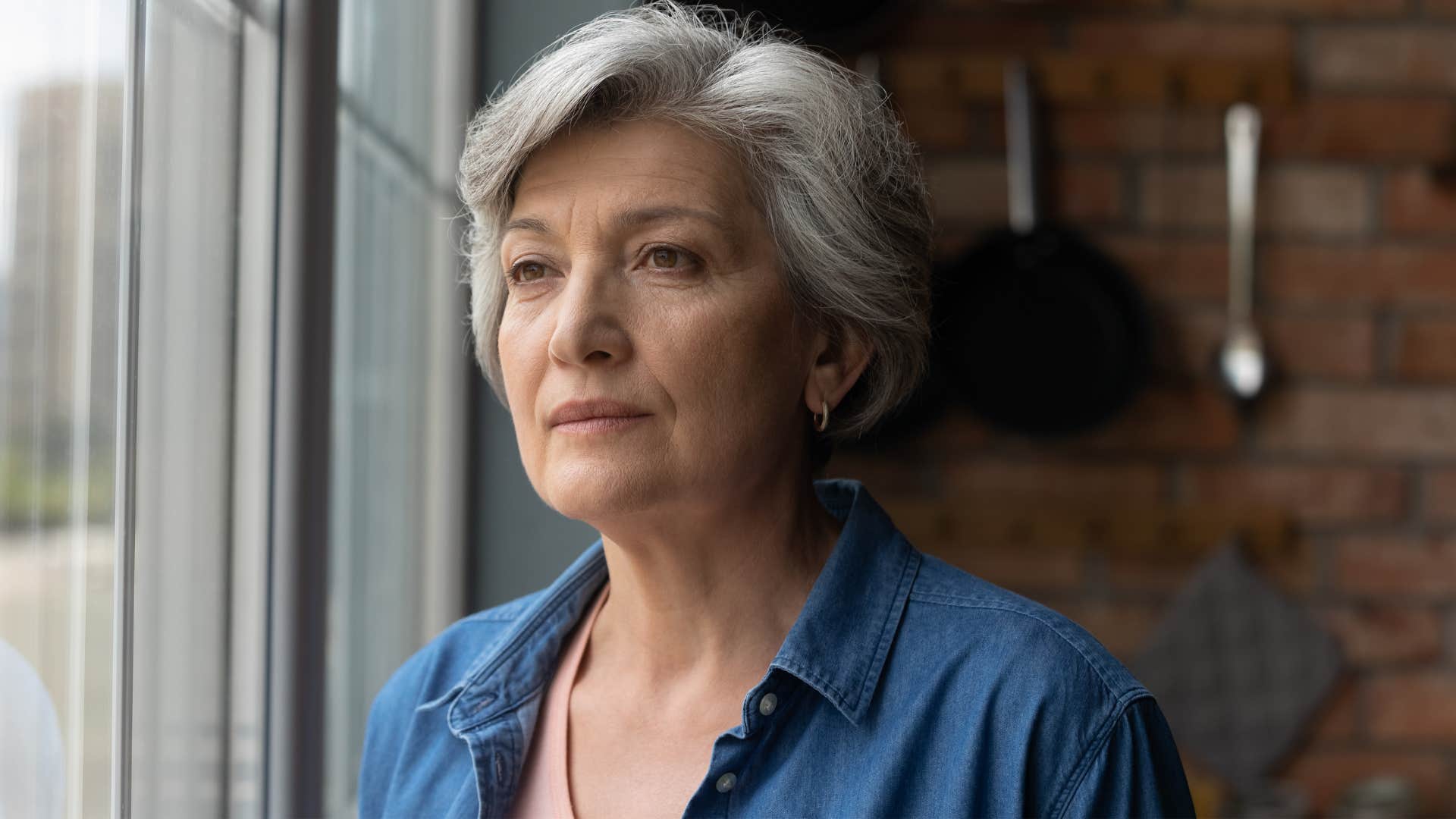 Older sad woman looking out of a window.