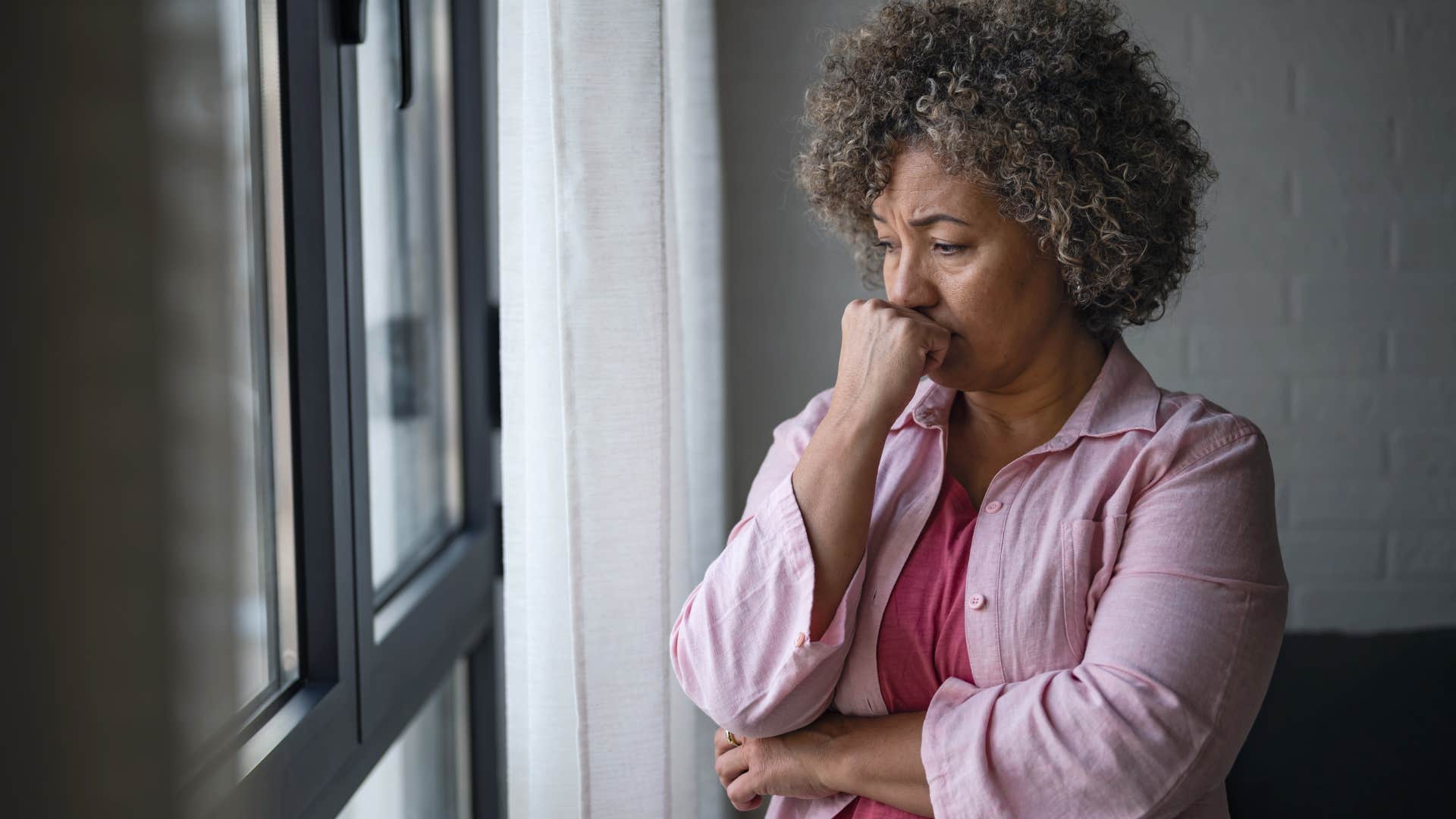 Older woman looking upset while staring out the window.