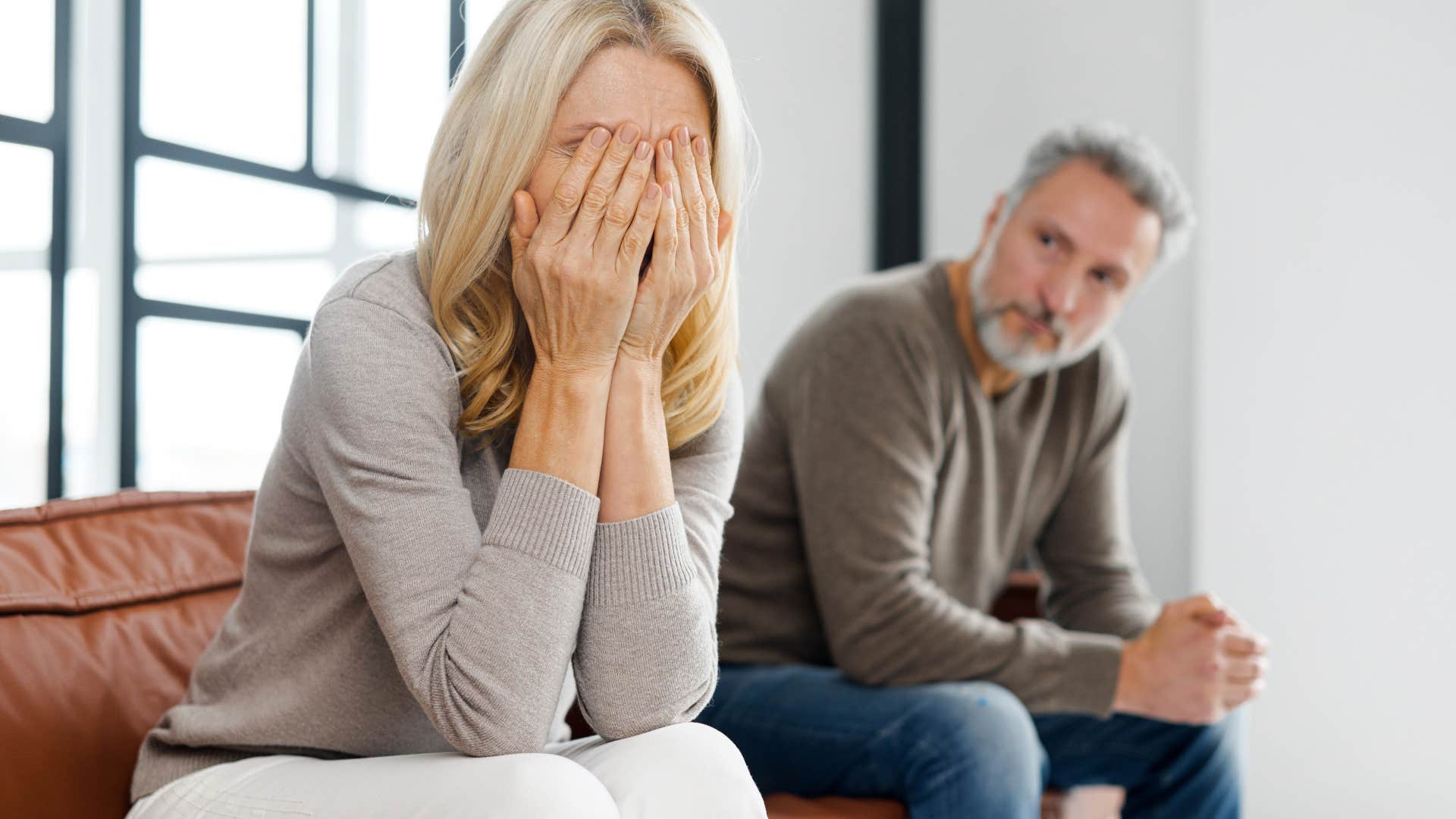 Woman holding her head in her hands with her partner sitting next to her. 