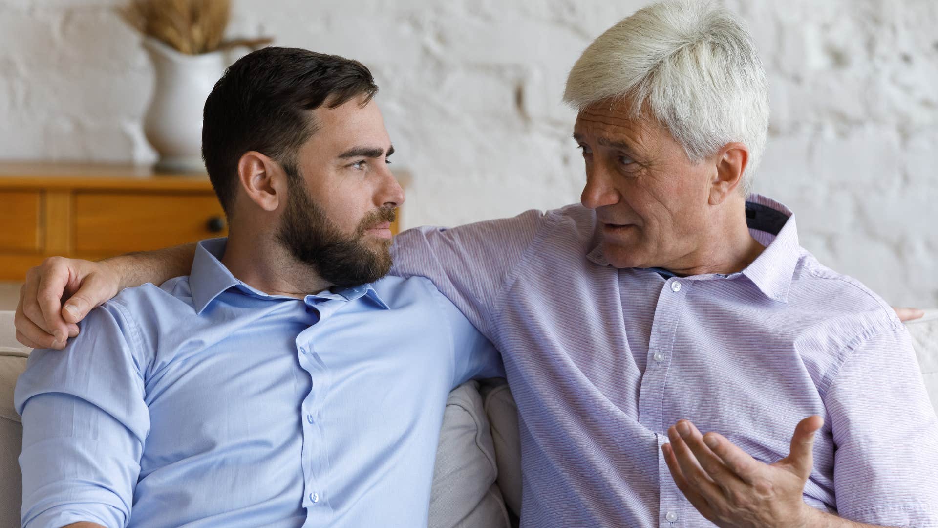 Older man talking to his adult son on the couch.