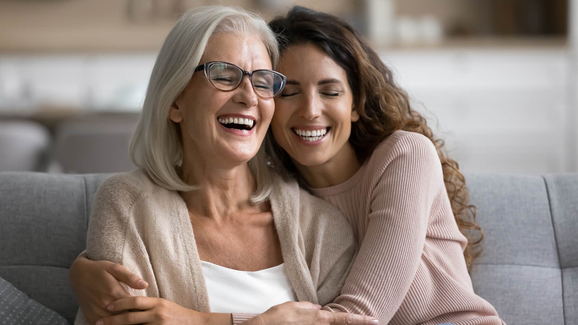 Adult daughter hugging her smiling mother on the couch.