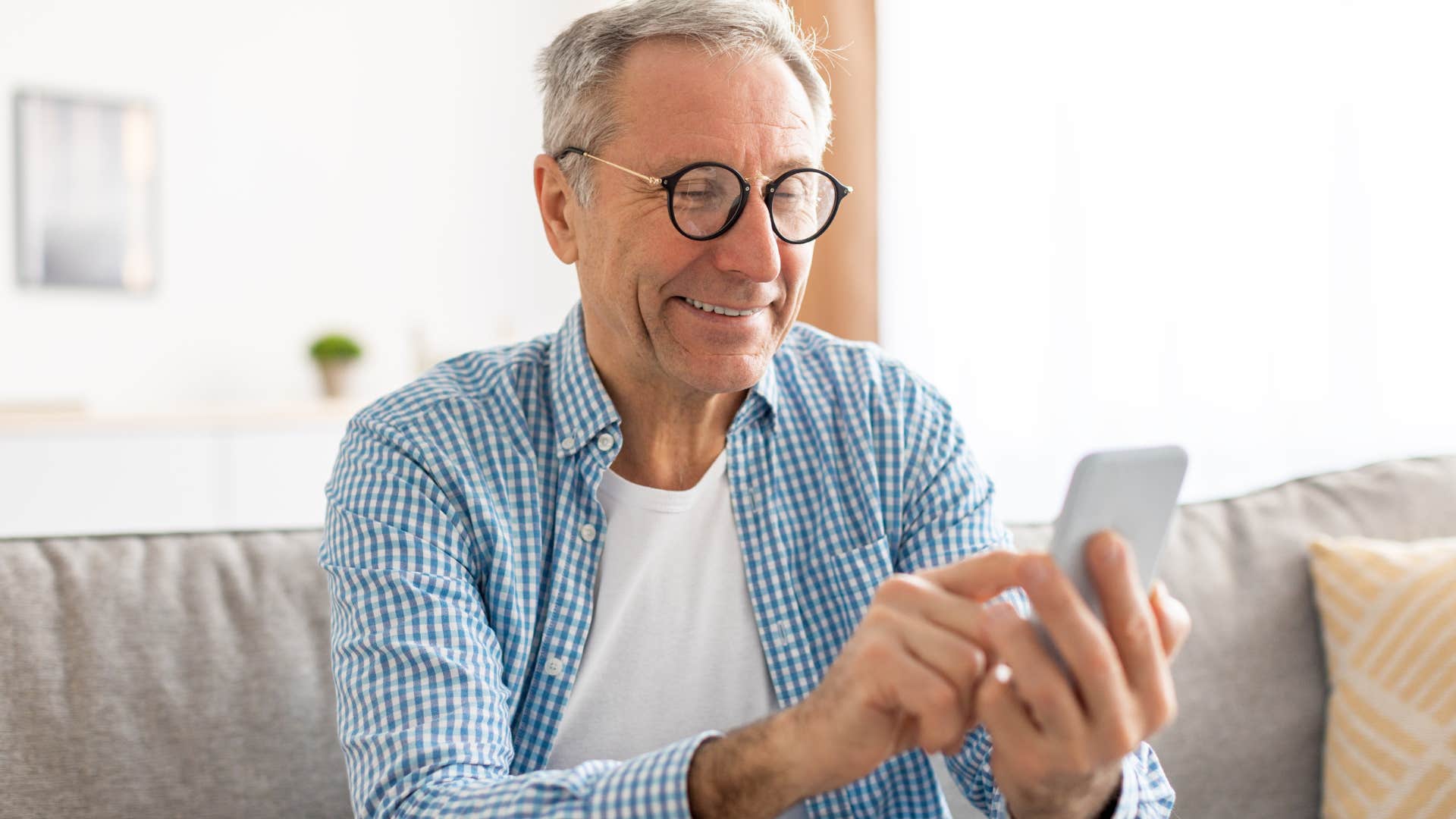 Older man smiling while typing on his cell phone.