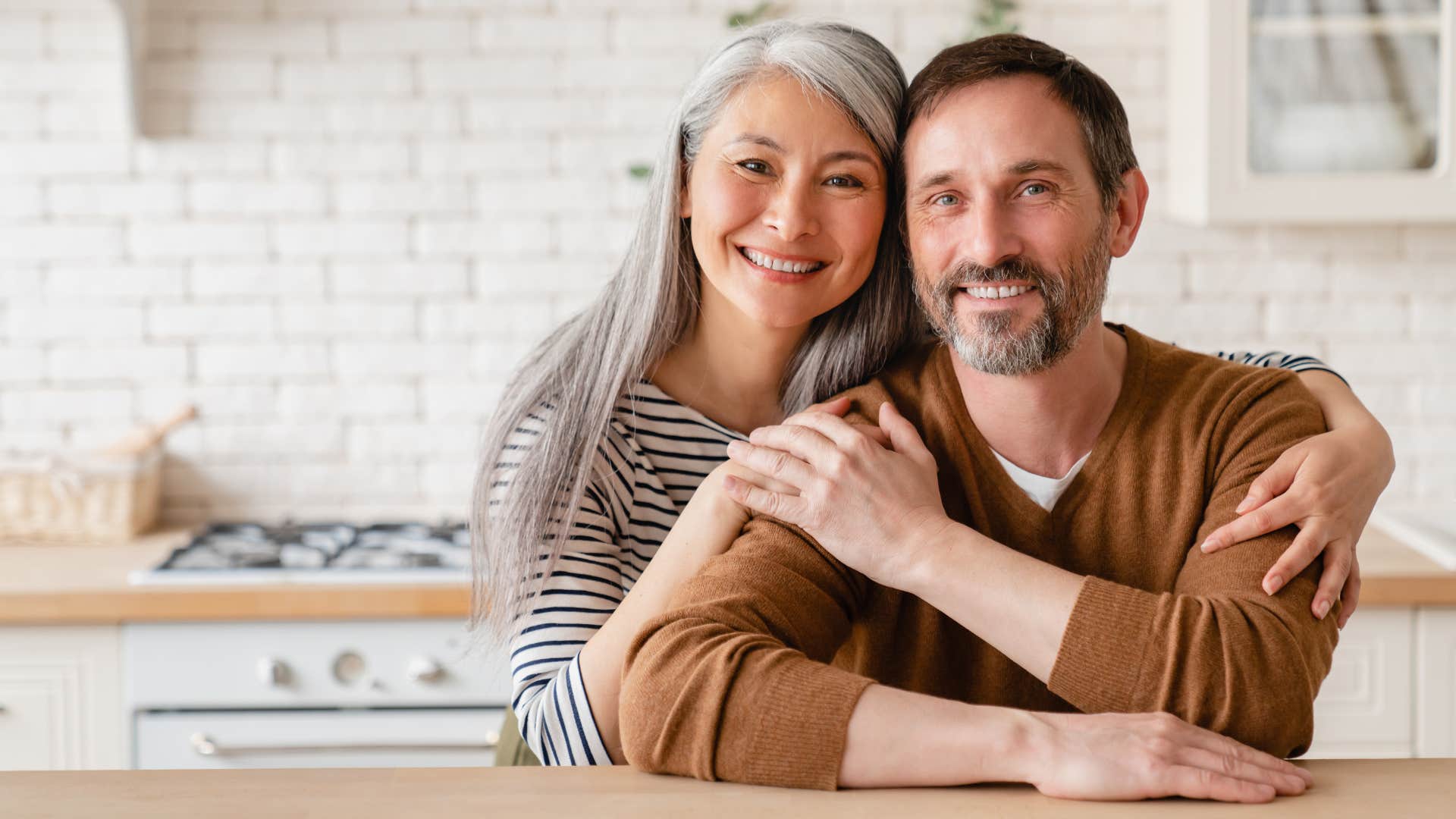 Older parents smiling and hugging each other in the kitchen.