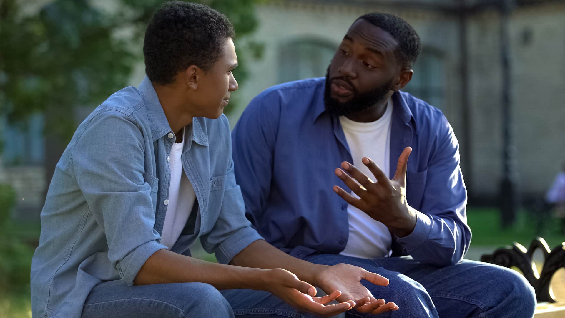 Dad talking to his teenage son on a bench.