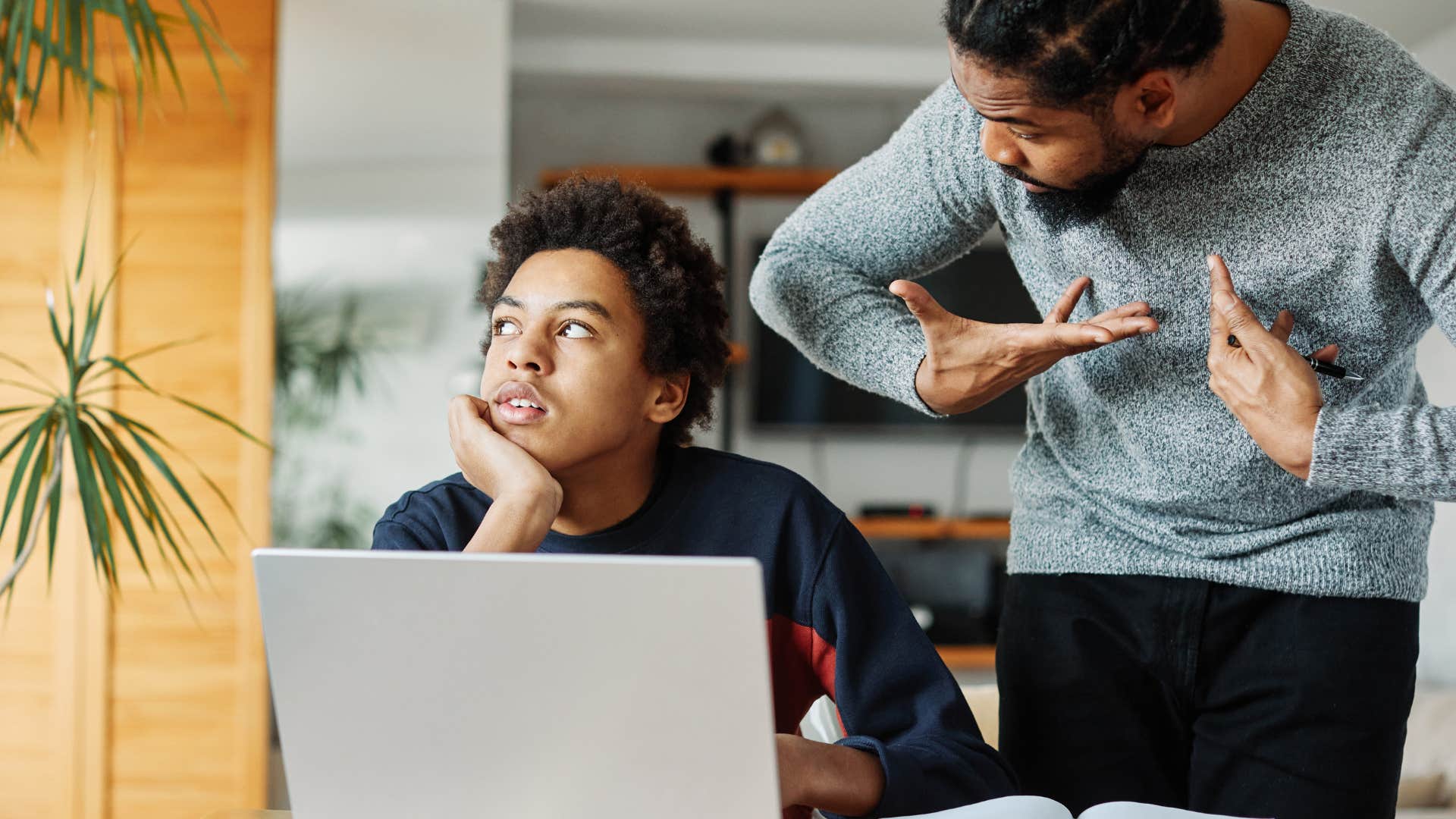 Teenager looking annoyed on his laptop while his dad yells at him.