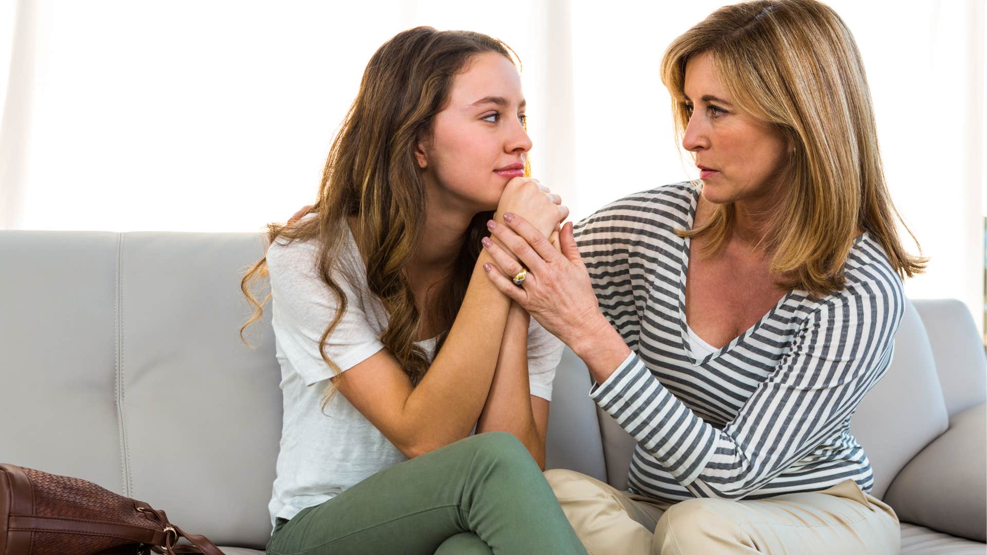 Mom comforting her annoyed teenage daughter on the couch.