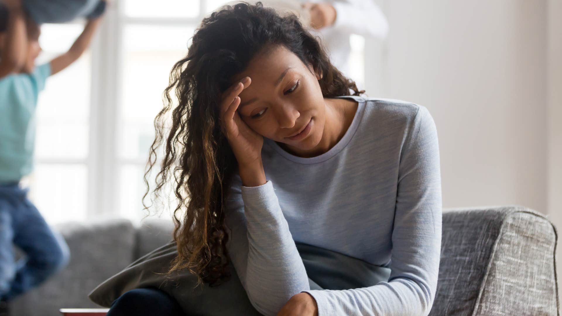 Woman looking stressed while her young kids play behind her.