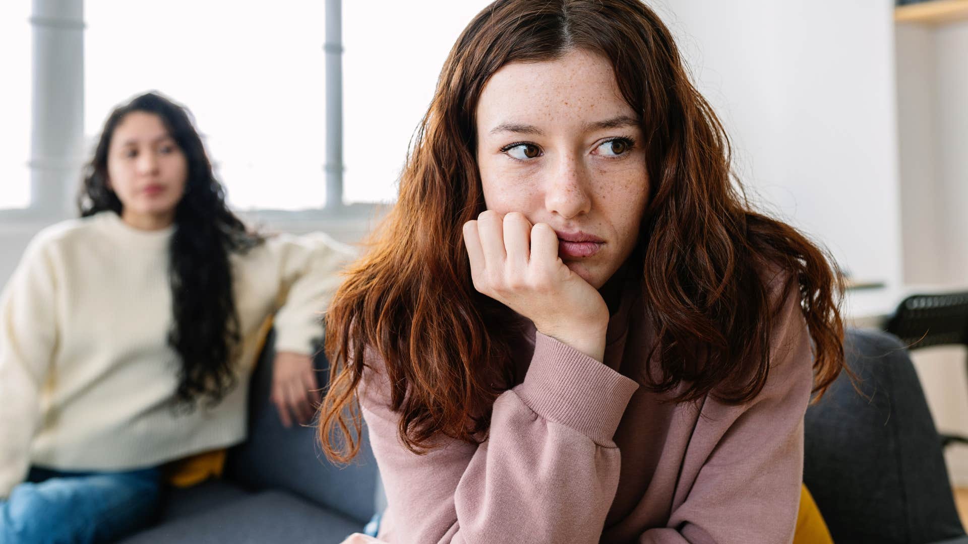 Young woman looking upset turned away from her friend on the couch.