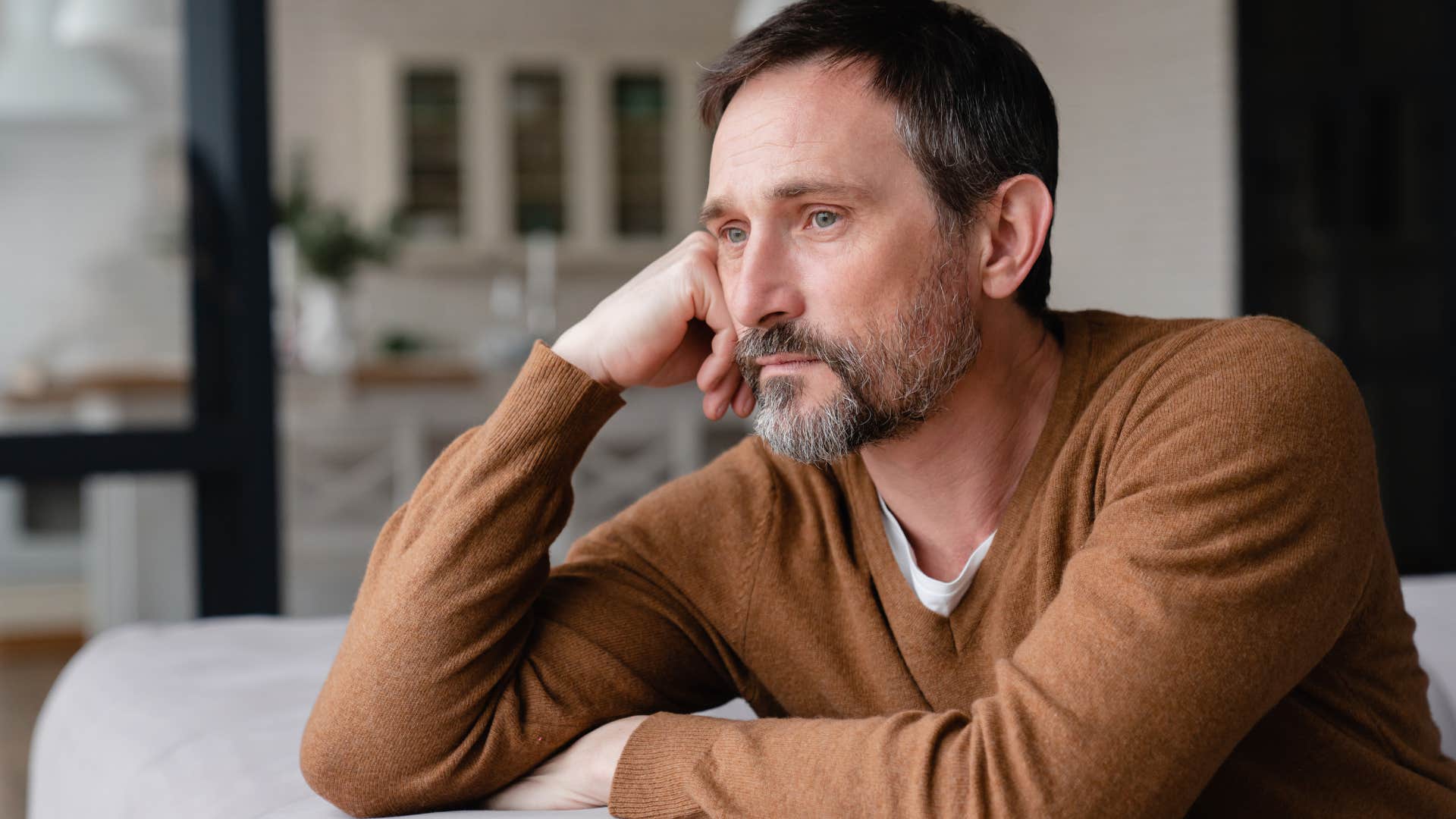 Older man looking upset staring out of a window.