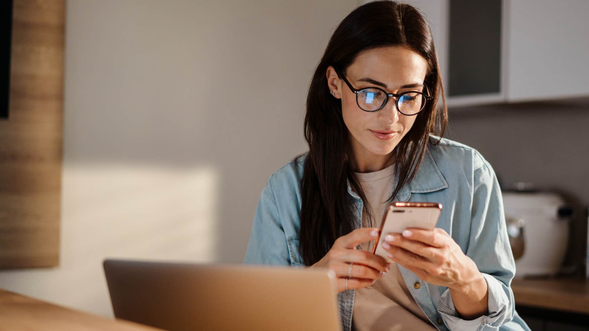 Woman staring at her phone in front of her laptop. 