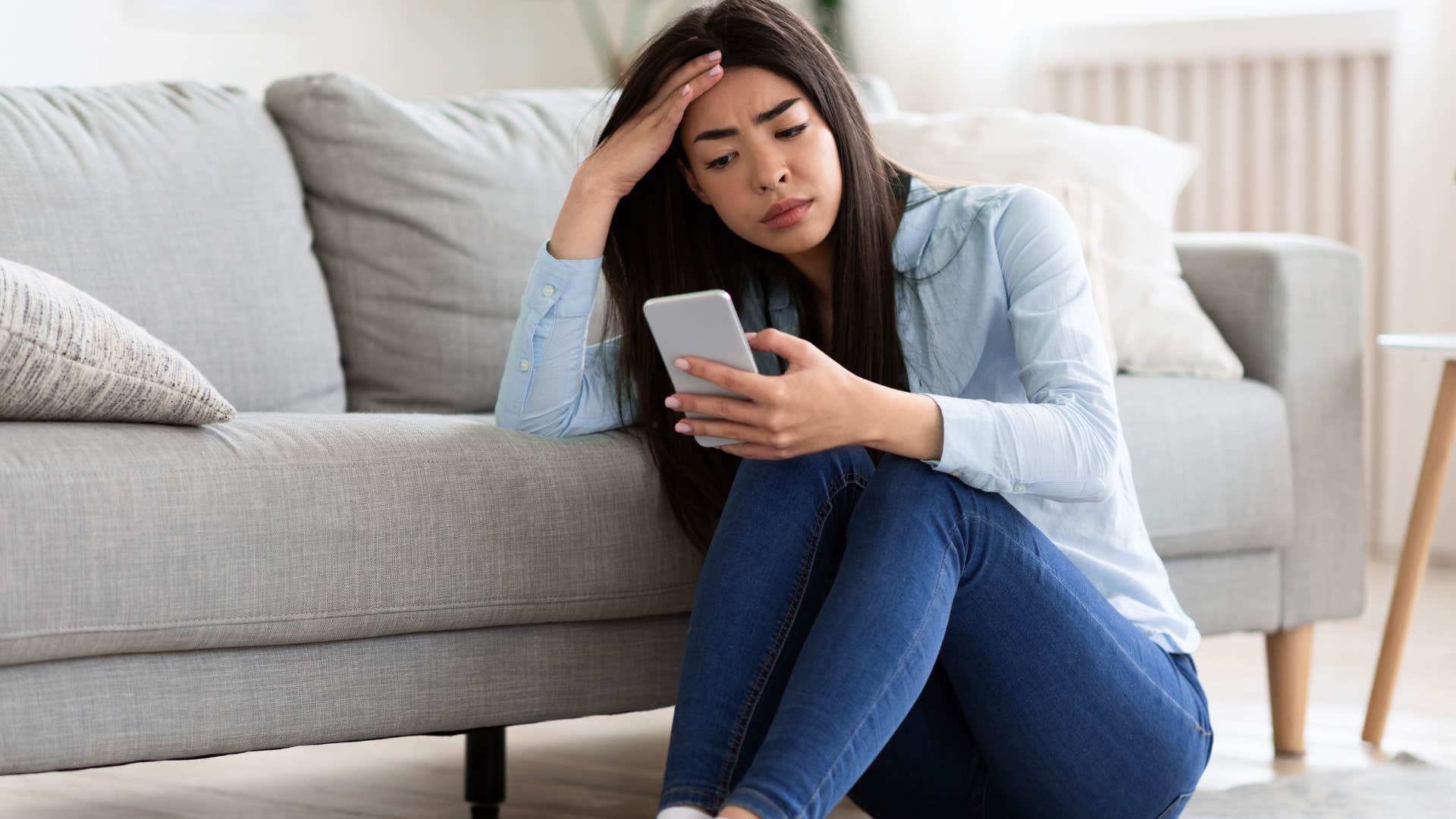 Woman looking upset staring at her phone on the couch.