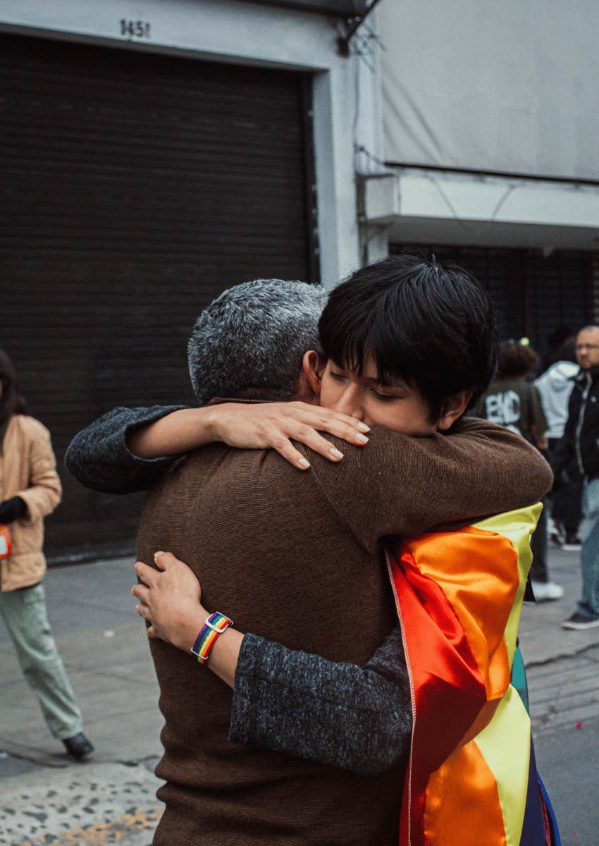 person wrapped in an lgbt flag hugging someone in public